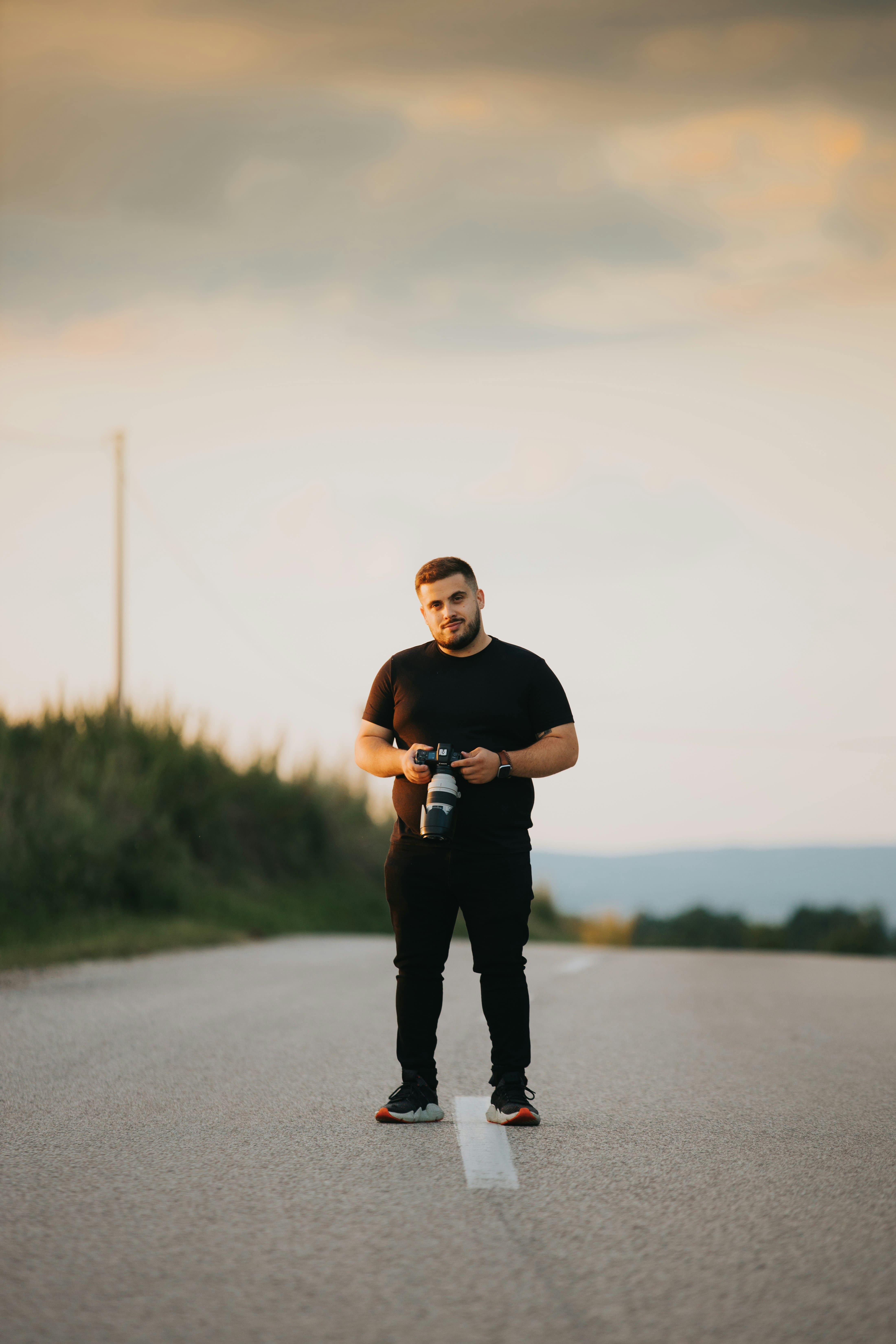 Un homme tenant un appareil photo et se tenant debout au milieu d'une route
